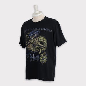 May include: Black t-shirt featuring a cartoon ram wearing a blue and white UNC hat. The text "Tar Heels" and "University of North Carolina" is printed on the shirt.