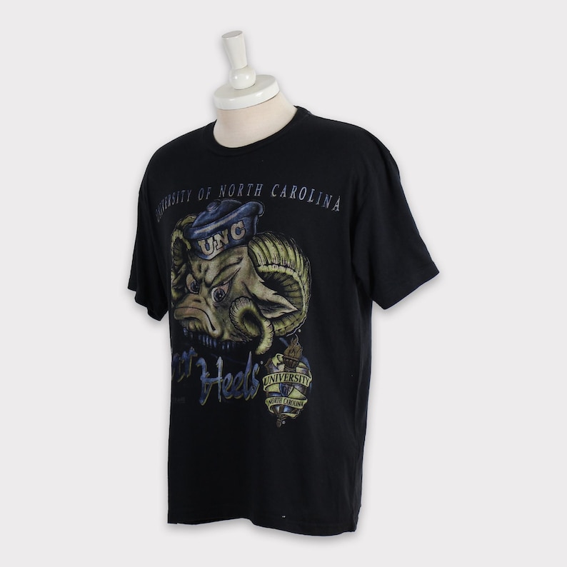 May include: Black t-shirt featuring a cartoon ram wearing a blue and white UNC hat. The text "Tar Heels" and "University of North Carolina" is printed on the shirt.