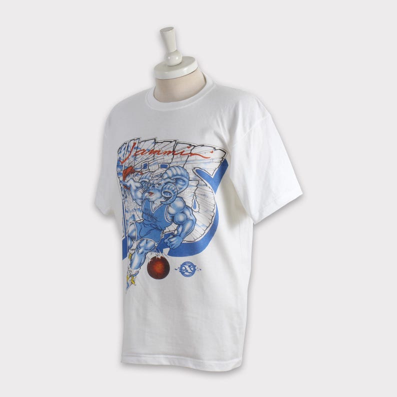 May include: White t-shirt featuring a muscular ram in a blue basketball uniform, holding a red ball. The graphic includes the word "Summit" and a blue and white design. The shirt is displayed on a mannequin.