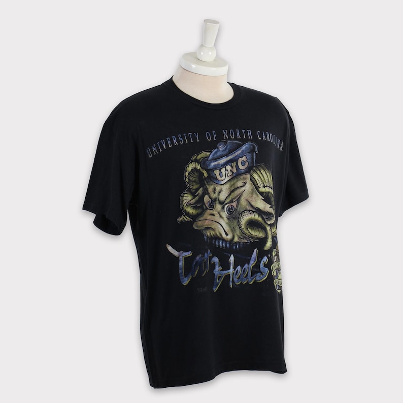 May include: Black t-shirt featuring a graphic of the University of North Carolina Tar Heels mascot, a ram wearing a sailor hat, and the text "Tar Heels" in a stylised font.