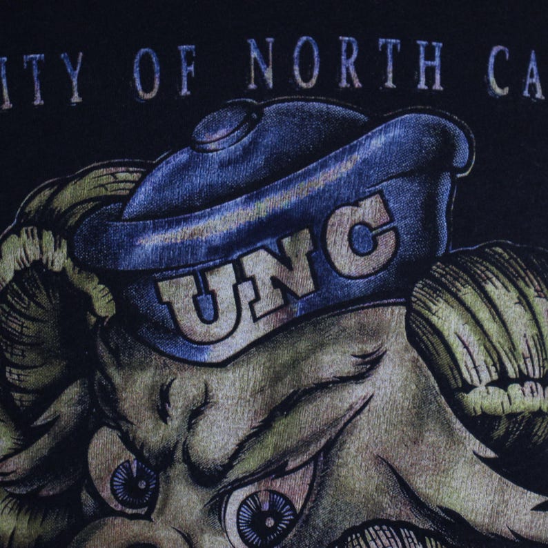 May include: A black t-shirt featuring a cartoon ram wearing a blue UNC hat. The text "University of North Carolina" is printed above the ram.