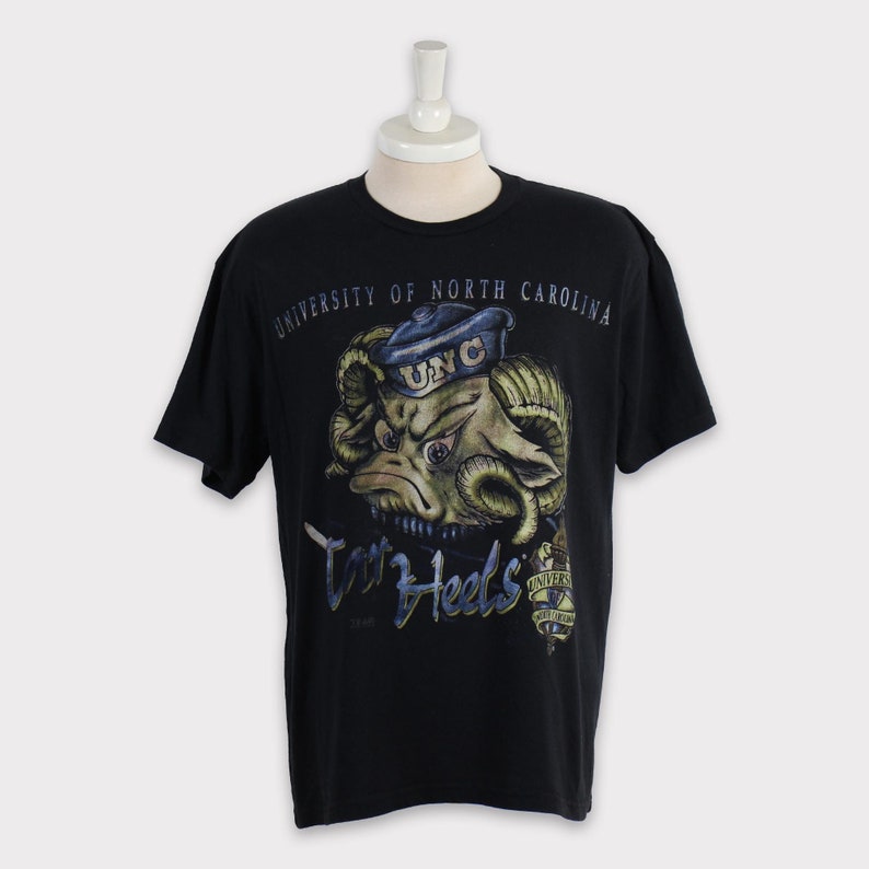 May include: Black t-shirt featuring a cartoon ram wearing a blue and white UNC hat. The text "University of North Carolina" and "Tar Heels" is printed on the shirt.