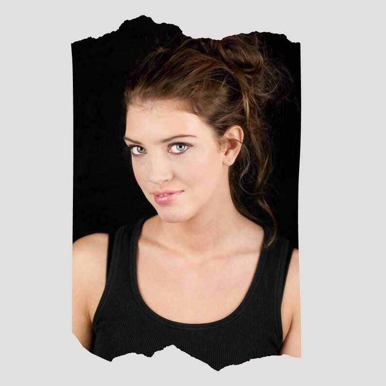 May include: A woman with long brown hair, wearing a black tank top, looks directly at the camera with a slight smile.