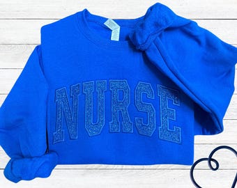 May include: A royal blue sweatshirt with the word "NURSE" in sparkly blue lettering.