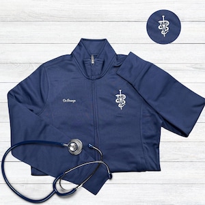 May include: Navy blue zip-up jacket with a white embroidered veterinary symbol and the text "Dr. Orange". A stethoscope is draped across the jacket. A matching patch with the veterinary symbol is in the upper right corner.