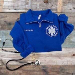 May include: Blue fleece pullover with a white embroidered star of life and the text "Emergency Department" and "Maddie, RN".