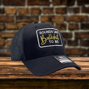 May include: A black mesh trucker hat with a white and yellow embroidered patch that says "Sounds Like Bullshit To Me".