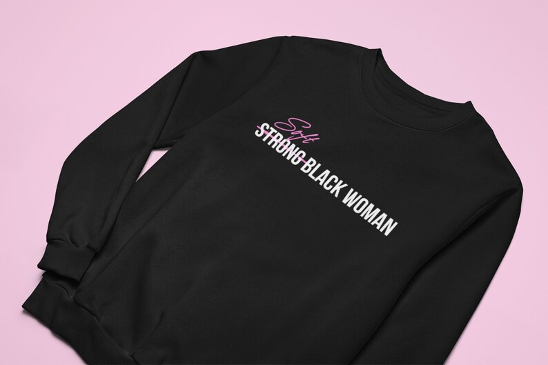 K&ouml;nnte beinhalten: Schwarzer Pullover mit wei&szlig;em Text, der "Soft Strong Black Woman" lautet, wobei das Wort "Soft" durchgestrichen ist. Das Wort "Soft" ist in Pink geschrieben.