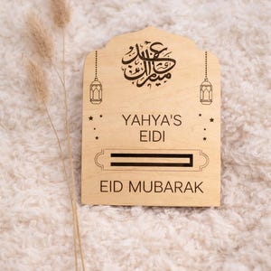 May include: A wooden Eid Mubarak gift box with the name "Yahya's" engraved. The box features Arabic calligraphy, star accents, and lantern designs. The text "EID MUBARAK" is also engraved on the box.