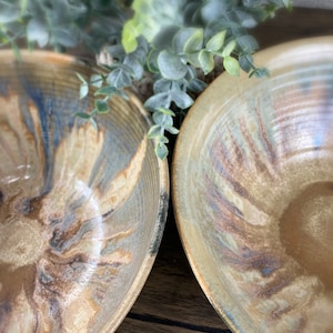 May include: Two ceramic bowls with a brown, blue, and white marbled glaze. The bowls are handmade and have a rustic, earthy look.
