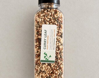 Op de afbeelding: Een doorzichtige plastic fles met een zwarte schroefdop gevuld met veelkleurige korrelige plantenvoeding. Een wit etiket op de voorzijde vermeldt CURRY LEAF PLANT FERTILIZER en de instructie om elke maand 2 eetlepels te gebruiken.