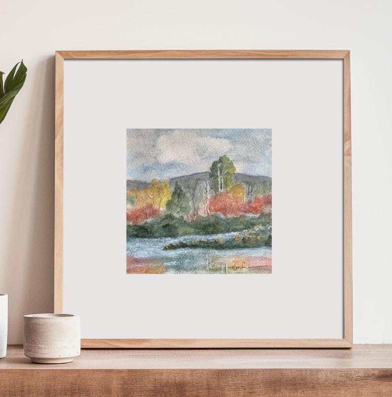 May include: Watercolor painting of a landscape with a lake, trees, and a cloudy sky. The trees are in shades of green, yellow, and red, and the lake is a light blue color.