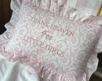 May include: A rectangular throw pillow with a ruffled edge, featuring a pink and white floral toile pattern. The center is embroidered with the text "THANK HEAVEN For LITTLE GIRLS" in pink thread, accompanied by a small pink heart icon.