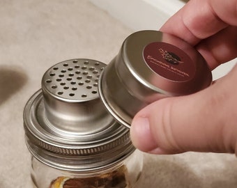 May include: A silver metal jar with a silver metal lid and a silver metal strainer lid. The jar has a brown label with the text "Epoché Infusions" on it.