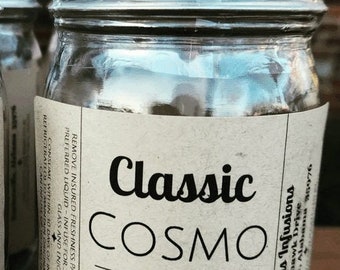 May include: A glass jar with a silver lid filled with dried fruit and sugar cubes. The label reads "Classic Cosmo Infusion Kit" and includes instructions to infuse for 3 days or heat the liquid first for 30 minutes. The ingredients are dehydrated lemons, limes, cranberries, and turbinado sugar cubes.