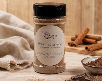 Könnte beinhalten: Ein durchsichtiges Gewürzglas aus Kunststoff mit schwarzem Deckel, das ein braunes Pulver enthält. Das Etikett trägt die Aufschrift Epicurious Infusions, Locally Made. Locally Loved. Cinnamon Chocolate Spice Mix und eine Kräuterabbildung.