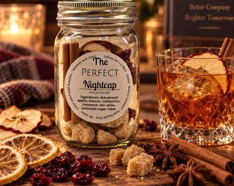 May include: A glass jar infusion kit labeled The PERFECT Nightcap containing dehydrated apples, lemons, cranberries, cinnamon, star anise, and turbinado sugar cubes. Next to it sits a glass of amber liquid with ice, a cinnamon stick, and an apple slice.