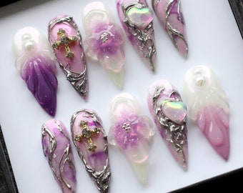 May include: Set of ten purple and white ombre press-on nails with silver and gold accents. Some nails feature a cross design, others have a flower design, and some have a heart design.