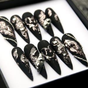 May include: Set of ten black stiletto false nails with silver and pink 3D embellishments. The nails have a textured, metallic finish.