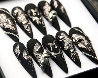 Puede incluir: Conjunto de diez uñas postizas stiletto negras con adornos 3D plateados y rosados. Las uñas tienen un acabado texturizado y metálico.