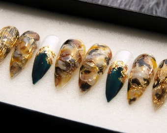 May include: Set of ten faux nail tips with a marbled design in shades of brown, white, and gold. The tips are accented with gold leaf and have a teal green base.