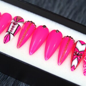 Puede incluir: Conjunto de diez u&ntilde;as postizas stiletto rosas con dise&ntilde;os geom&eacute;tricos blancos y negros y pedrer&iacute;a.
