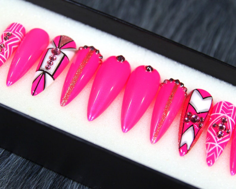 Puede incluir: Conjunto de diez u&ntilde;as postizas stiletto rosas con dise&ntilde;os geom&eacute;tricos blancos y negros y pedrer&iacute;a.