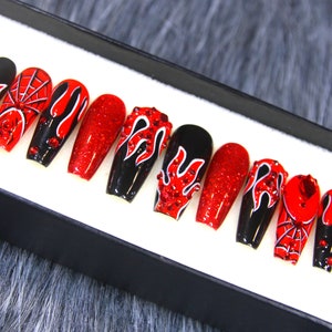 May include: Set of ten red and black coffin-shaped false nails with a variety of designs, including flames, spiderwebs, and rhinestones.
