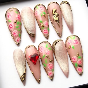 May include: Set of ten long, almond-shaped false nails with a pink base and gold accents. Some nails feature a floral design with pink roses and green leaves, while others have a glitter finish or a single red heart.