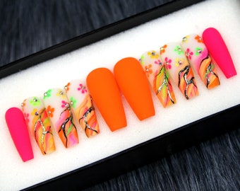 May include: Set of ten false nails with a bright orange and pink color scheme. The nails feature a white base with a floral design and silver accents.