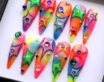 May include: Set of ten colorful fake nails with a tie-dye effect and star designs. Each nail is decorated with rhinestones.