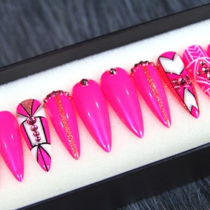 Puede incluir: Conjunto de diez u&ntilde;as postizas stiletto rosas con dise&ntilde;os geom&eacute;tricos blancos y negros y pedrer&iacute;a.