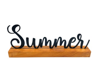 Puede incluir: Corte de metal negro de la palabra "Summer" sobre una base de madera.