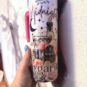 May include: A cylindrical tumbler with a pink handle featuring a graphic print of a tequila bottle, a margarita glass with lime, a black candle, and roses. The text reads Plant lavender for luck, Midnight, Tequila, and Margarita.