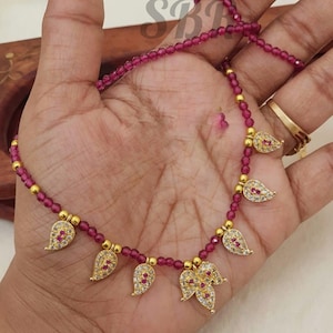 May include: A pink beaded necklace with gold leaf pendants adorned with clear rhinestones.