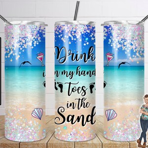 May include: Two stainless steel tumblers with a glitter finish and a beach scene design. The tumblers feature the text "Drink in my hand, toes in the sand".