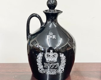 Puede incluir: Decantador de cerámica negra con un diseño plateado que presenta una corona y el texto "E.R. 1977 The Queen's Silver Jubilee".