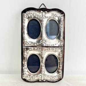 May include: A rectangular silver-toned wall-hanging frame featuring four oval-shaped openings arranged in two rows. The frame is decorated with embossed floral and ribbon motifs and is mounted on a dark brown velvet backing with a metal hanging loop.