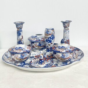 May include: A collection of blue and white porcelain tableware with an Asian-inspired design. The set includes a serving tray, two covered bowls, a vase, two candlesticks, and a small ring holder. The design features red and gold accents.