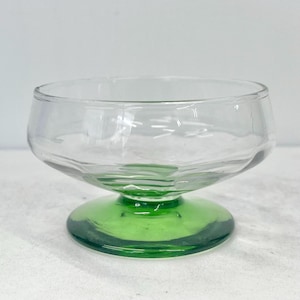 以下が含まれることがあります： 緑色の台座が付いた透明なガラス製のデザート皿。皿は波状の縁と広く浅いボウルを持っています。