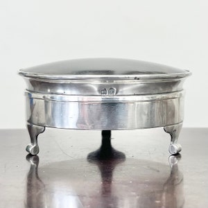 May include: A silver magnifying glass with a round, black glass lens. The magnifying glass is on three legs and has a silver band around the base.