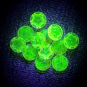 May include: A group of 10 vintage green glass buttons with a starburst design. The buttons are arranged in a pile on a dark blue fabric background.