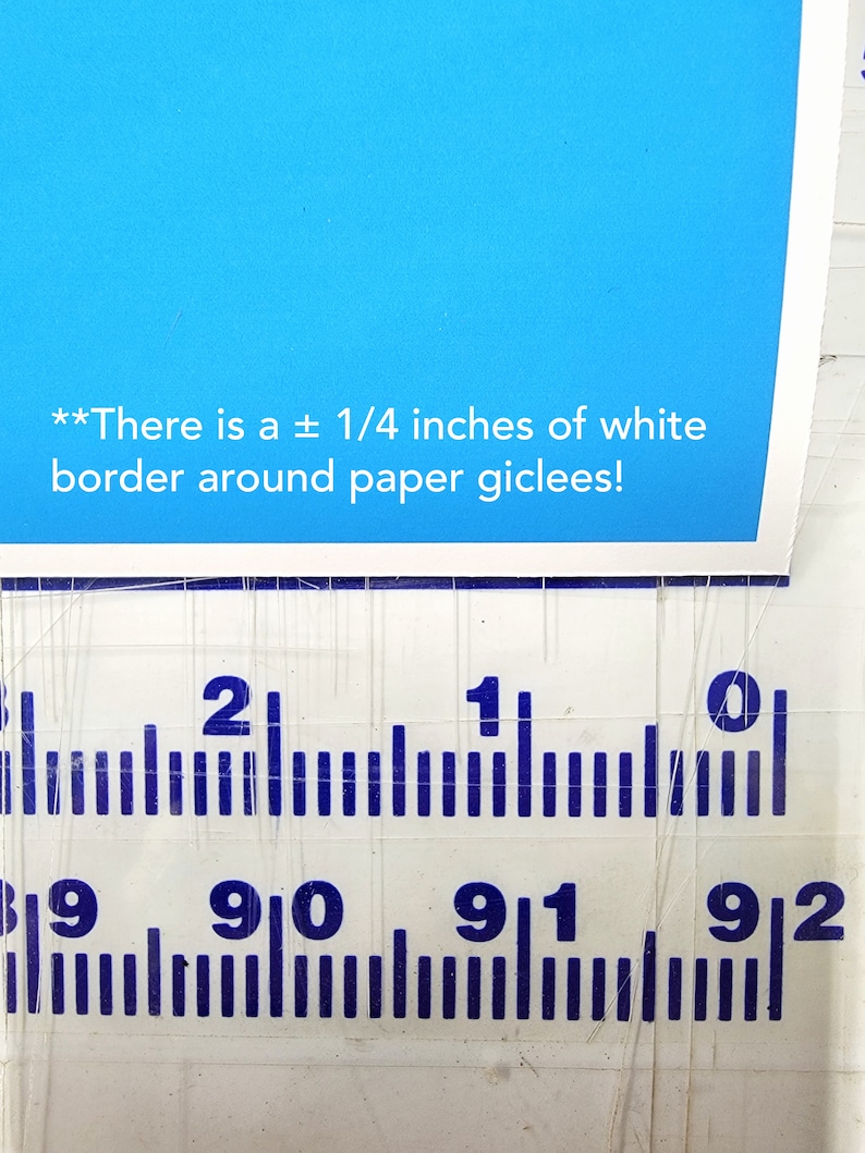 Puede incluir: Un primer plano de una regla con marcas azules que muestran medidas en pulgadas. El texto "There is a &plusmn; 1/4 inches of white border around paper giclees!" es visible en la parte superior de la imagen.