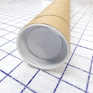 Puede incluir: Un tubo de cart&oacute;n marr&oacute;n con una tapa de pl&aacute;stico blanco. El tubo est&aacute; sobre una superficie blanca con un patr&oacute;n de cuadr&iacute;cula azul.