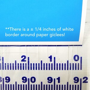 May include: A close-up of a ruler with blue markings showing measurements in inches. The text "There is a &plusmn; 1/4 inches of white border around paper giclees!" is visible at the top of the image.
