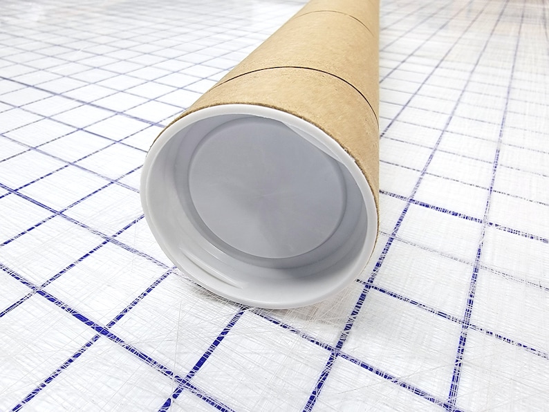 May include: A brown cardboard tube with a white plastic end cap. The tube is lying on a white surface with a blue grid pattern.