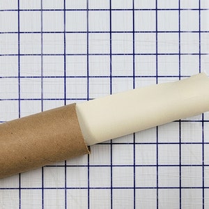 Puede incluir: Un lienzo de pintura enrollado se guarda en un tubo de cart&oacute;n marr&oacute;n. El tubo est&aacute; sobre una superficie blanca cuadriculada.