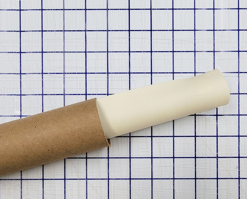 Puede incluir: Un lienzo de pintura enrollado se guarda en un tubo de cart&oacute;n marr&oacute;n. El tubo est&aacute; sobre una superficie blanca cuadriculada.