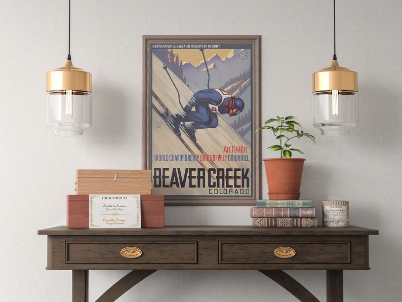 May include: A vintage poster advertising Beaver Creek, Colorado, a ski resort in the Rocky Mountains. The poster features a skier in a blue and red suit, a mountain landscape, and the text "North America's Grand Mountain Resort", "Alt. 11,440 ft.", "World Championship Birds of Prey Downhill", "Beaver Creek", and "Colorado".