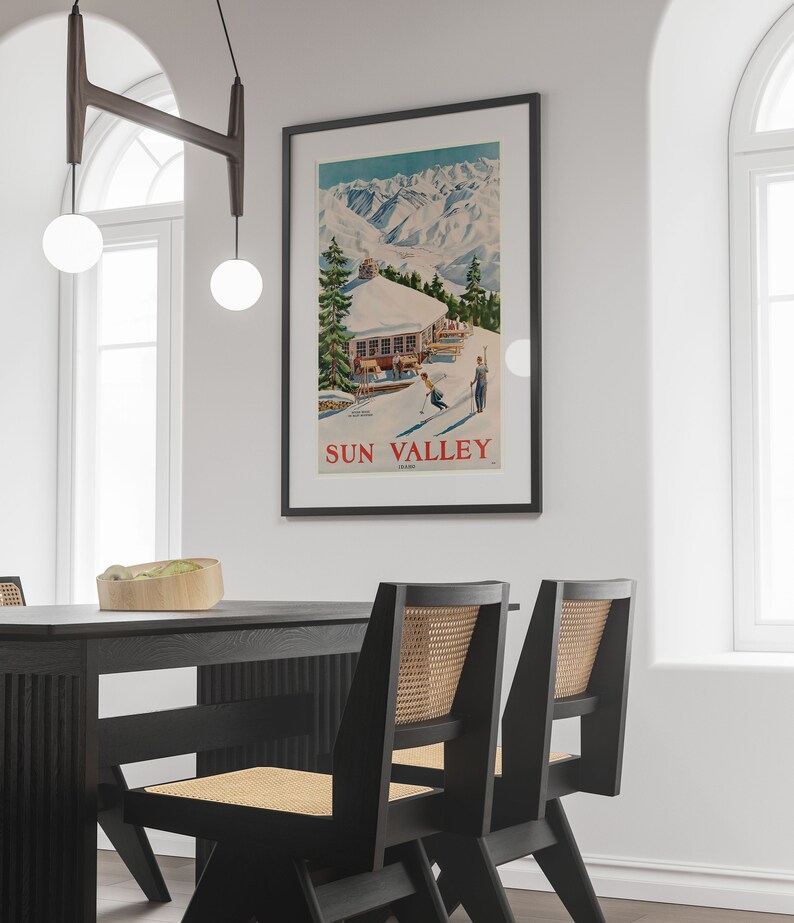 Puede incluir: Un cartel vintage que anuncia Sun Valley, Idaho, con una ilustraci&oacute;n colorida de un albergue de esqu&iacute; y esquiadores en una ladera de monta&ntilde;a nevada.